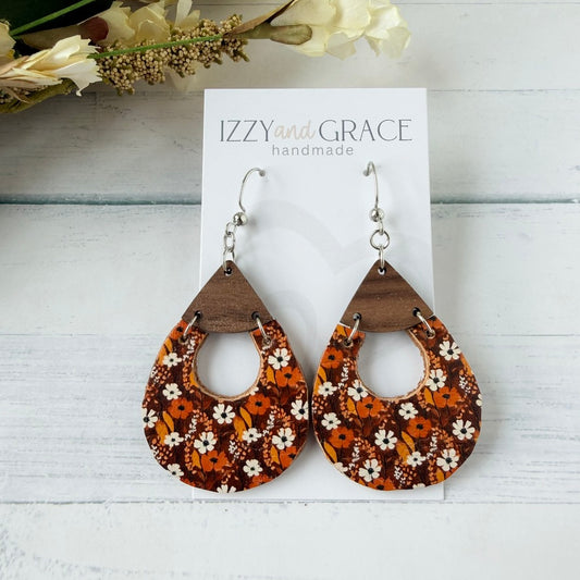 Teardrop-shaped wooden dangle earrings with a brown and orange floral pattern, displayed on a white card labeled 'IZZY and GRACE handmade' on a white wood background.
