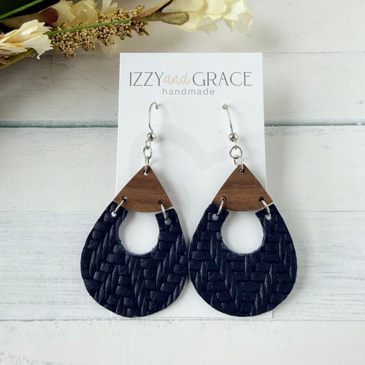 A pair of teardrop-shaped dangle earrings with dark navy woven leather and natural wood triangle tops, hanging from silver fishhook wires on a white display card labeled 'IZZYandGRACE handmade'.