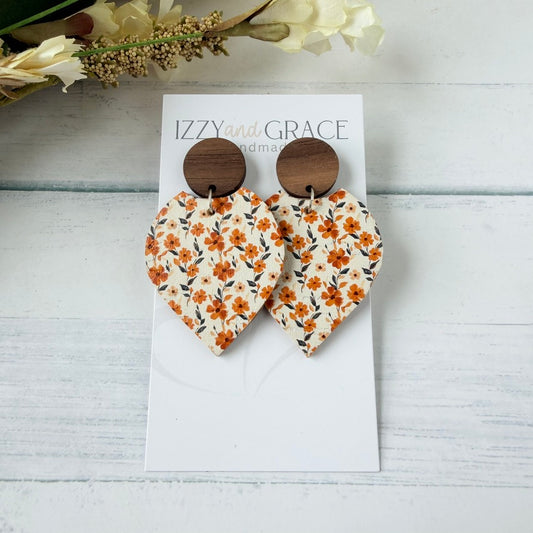petal-shaped dangle earrings with a white leather printed with orange and flowers, featuring round wooden studs, displayed on a white card labeled 'IZZY and GRACE'.