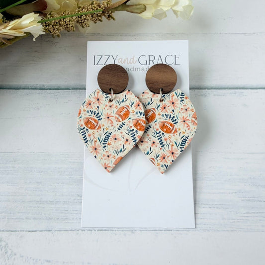 A pair of petal-shaped dangle earrings displayed on a white card. The earrings feature a floral leather pattern with brown football motifs and are finished with round wooden studs.