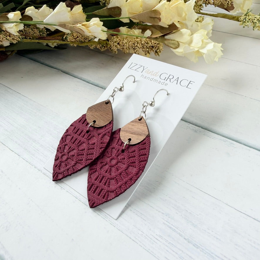 A pair of handmade dangle earrings displayed on a white card labeled 'Izzy and Grace handmade.' The earrings have a burgundy leather embossed lower section and a light brown wooden upper section with silver-tone hooks.