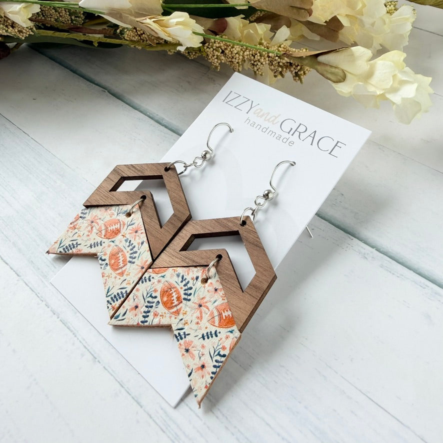 Geometric dangle earrings with a natural wood frame and a floral chevron pattern in orange, beige, and green, displayed on a white card labeled 'IZZYand GRACE handmade' on a white wood background.
