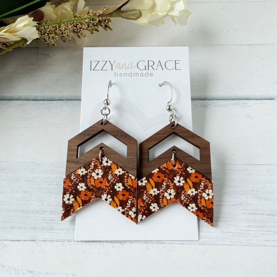 Wooden geometric dangle earrings with a brown wood grain frame and a triangular drop featuring a white, orange, and brown floral pattern, displayed on a white card labeled 'Izzy and Grace handmade'.