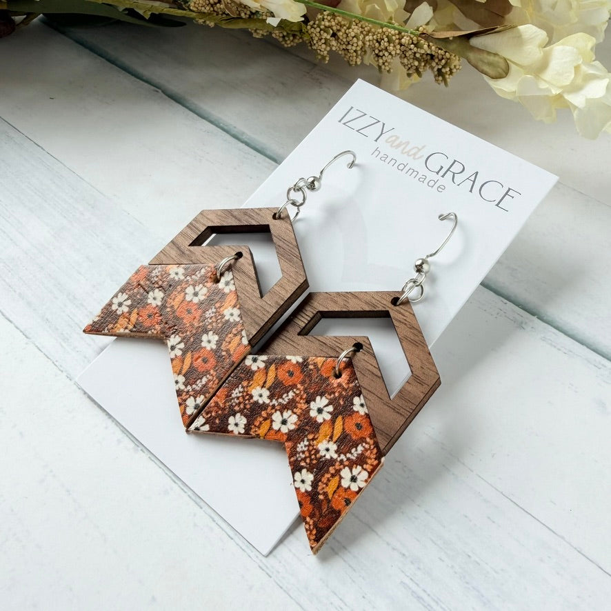 Wooden geometric dangle earrings with a brown wood grain frame and a triangular drop featuring a white, orange, and brown floral pattern, displayed on a white card labeled 'Izzy and Grace handmade'.