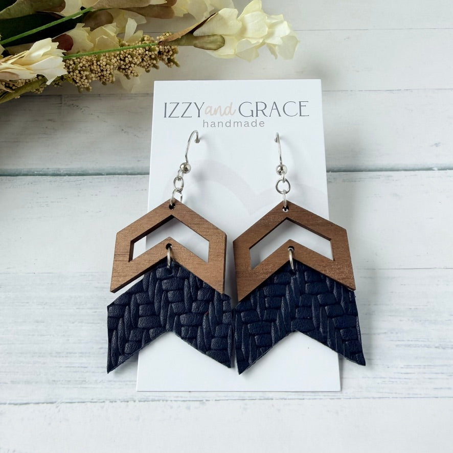 A pair of geometric drop earrings displayed on a white card labeled 'IZZY and GRACE handmade.' The earrings have a medium brown wood geometric top and a dark navy woven geometric bottom, hanging from silver hooks.