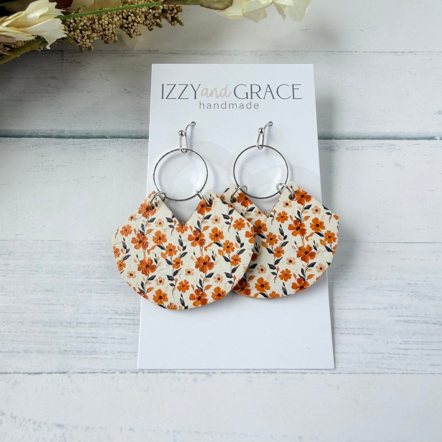 A pair of handmade dangle earrings displayed on a white card labeled 'IZZY and GRACE handmade.' The earrings have silver-tone hoop tops and fan-shaped lower pieces printed with an orange, white, and dark floral pattern.