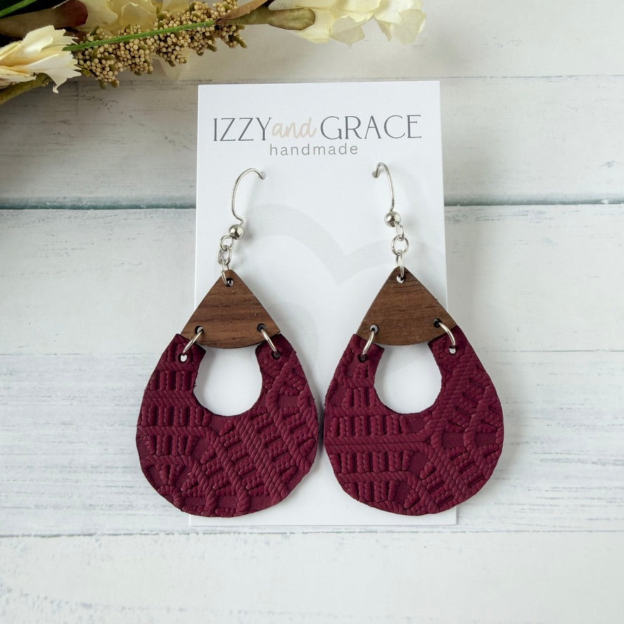 A pair of handmade teardrop dangle earrings displayed on a white card labeled 'IZZY and GRACE handmade.' The earrings have silver fishhook wires, triangular medium-brown wood tops, and textured deep burgundy lace-like lower halves.