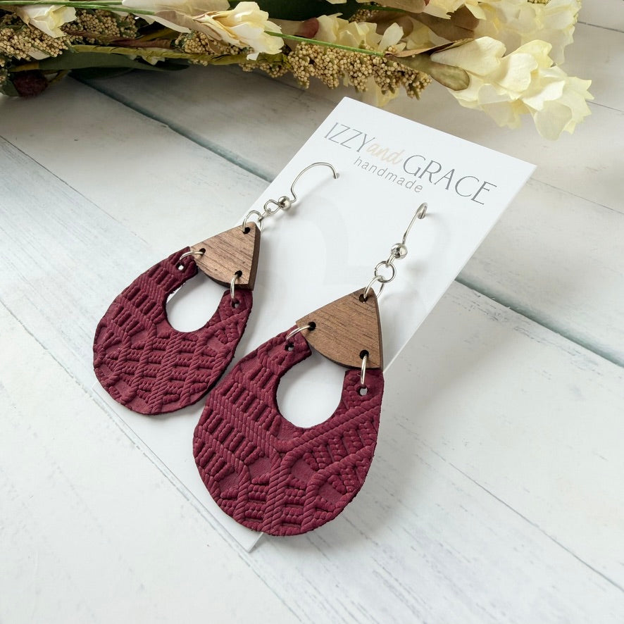 A pair of handmade dangle earrings displayed on a white card labeled 'IZZY and GRACE handmade'. The earrings feature a deep burgundy lace-textured teardrop drop with a small triangular wooden accent at the top and silver-tone hooks.