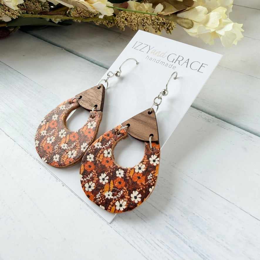 A pair of teardrop-shaped wooden dangle earrings with a brown and orange floral pattern, displayed on a white card labeled 'VZZYandGrace handmade' on a white wooden surface.