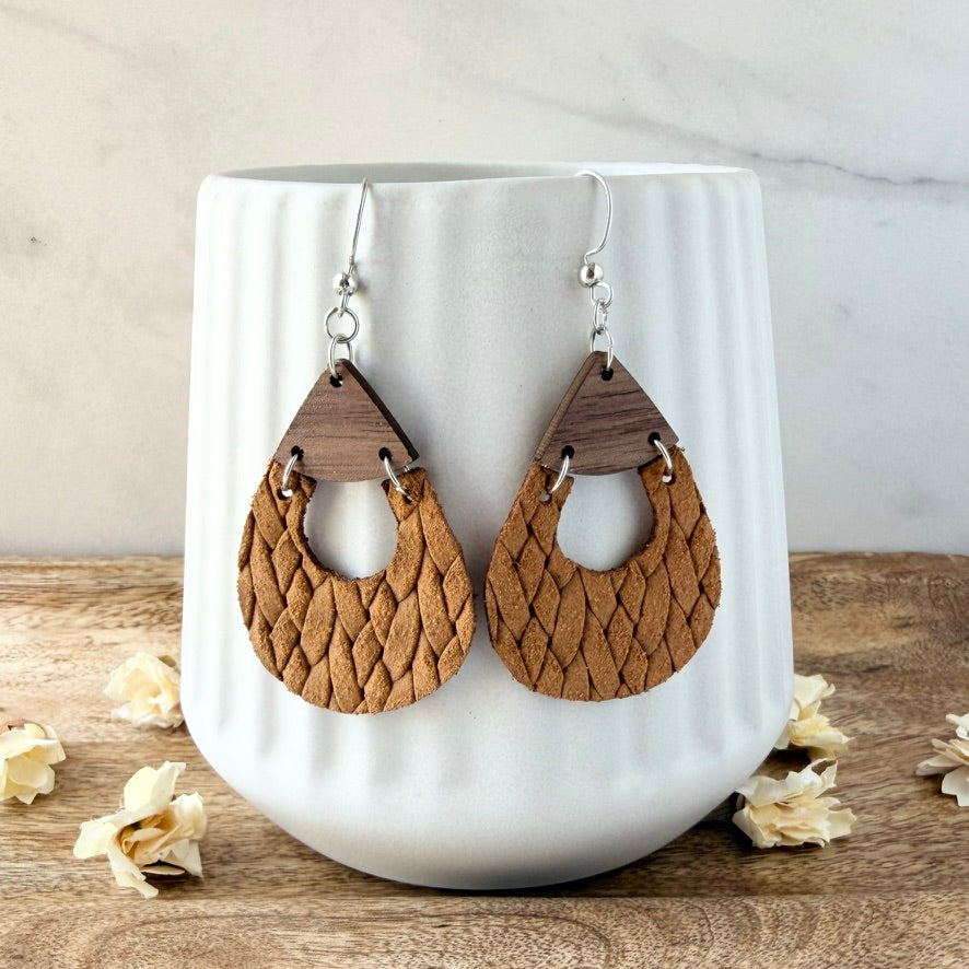 A pair of teardrop-shaped wooden dangle earrings with a textured woven pattern, displayed on a white ribbed ceramic vase.