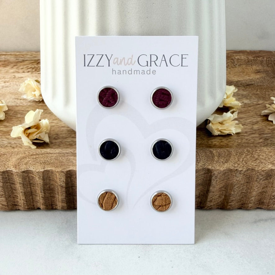 A set of six round stud earrings displayed on a white card labeled 'IZZY and GRACE handmade.' The earrings feature alternating deep burgundy, black, and natural wood tones, set in silver-toned metal.