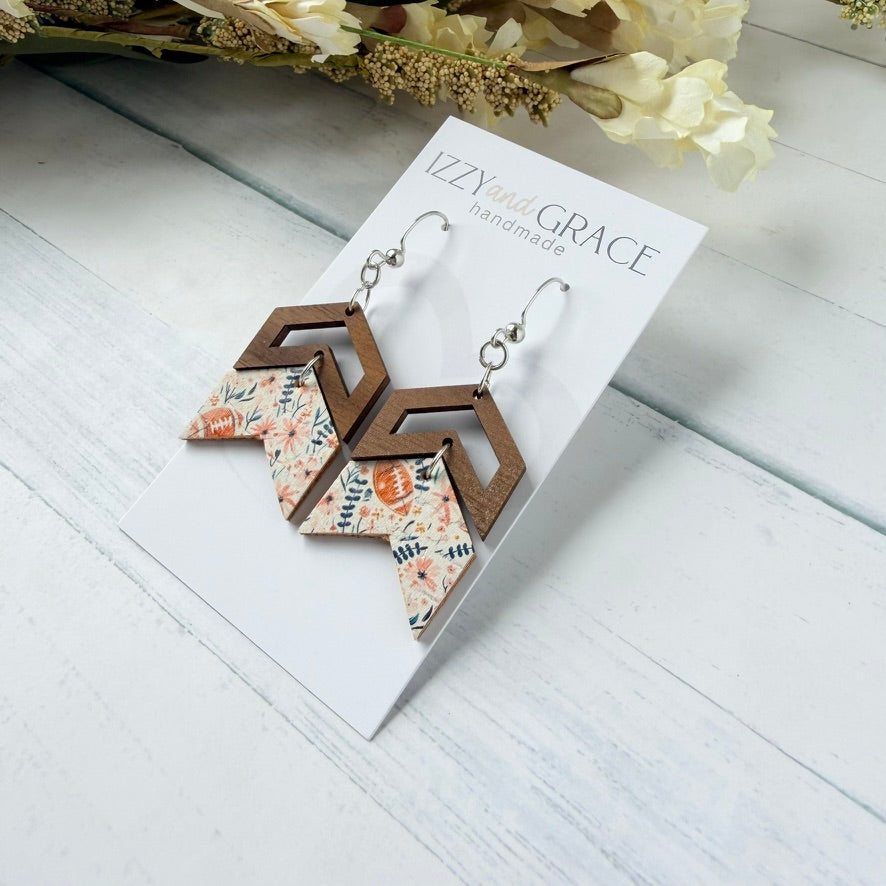Geometric wooden dangle earrings with floral patterned paper inserts, displayed on a white card labeled 'Izzy's Grace handmade' on a white wood surface with dried flowers in the background.