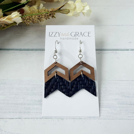 A pair of geometric dangle earrings displayed on a white card labeled 'IZZY and GRACE handmade.' The earrings have a dark navy woven lower section and a light brown wood upper section with an open chevron design.