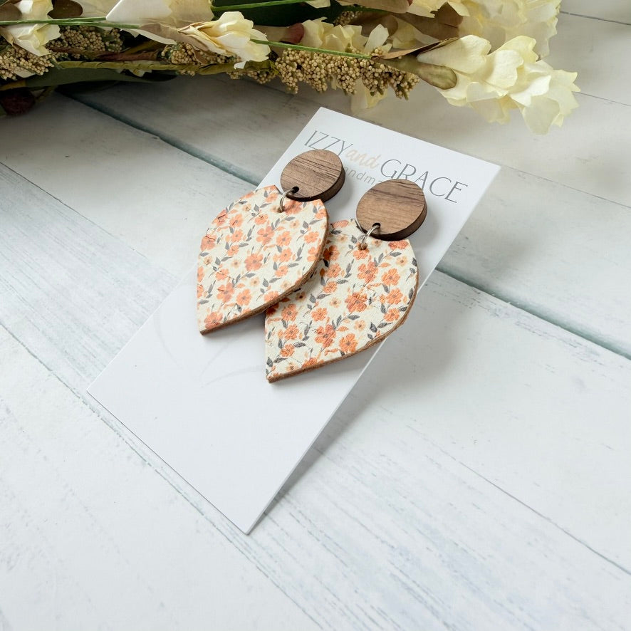petal-shaped dangle earrings with a peach and orange floral pattern on a cream background, hanging from round wooden studs, displayed on a white card labeled 'Izzy in Grace' on a white wood plank surface.