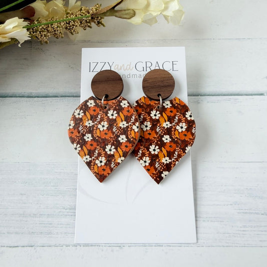 A pair of wooden drop earrings with a brown and orange floral patterned petal-shaped dangle, displayed on a white card labeled 'IZZY and GRACE handmade' on a light wood background.