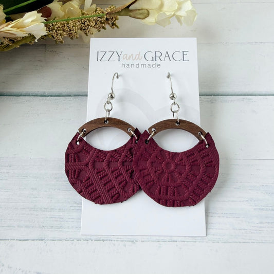 A pair of handmade dangle earrings displayed on a white card labeled 'IZZY and GRACE handmade.' The earrings have textured burgundy circular drop sections with brown wooden arches and silver fishhook wires.