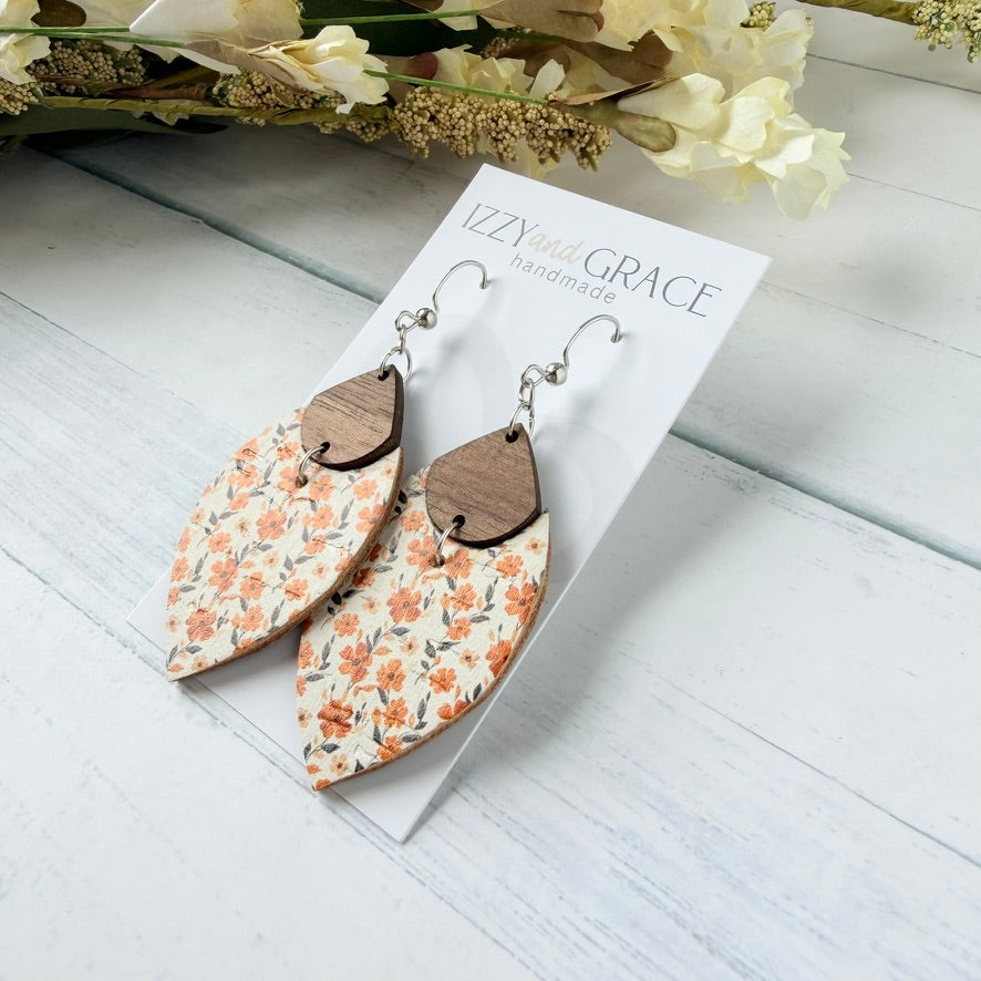 A pair of handmade dangle earrings displayed on a white card labeled 'Izzy and Grace handmade.' The earrings have a cream background with a small orange floral pattern and a dark brown wooden teardrop-shaped top, hanging from silver fishhook wires.