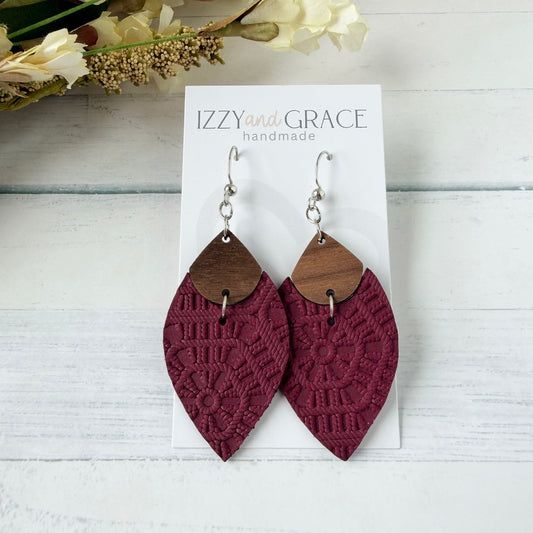 A pair of petal-shaped dangle earrings displayed on a white card labeled 'IZZY and GRACE handmade.' The earrings have silver hooks, medium brown wooden top sections, and textured burgundy lower sections with an embossed pattern.