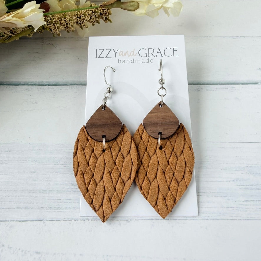 A pair of mustard woven leather dangle earrings with dark wood top caps and silver fishhook wires, displayed on a white card labeled 'IZZY and GRACE handmade' on a white wood background.