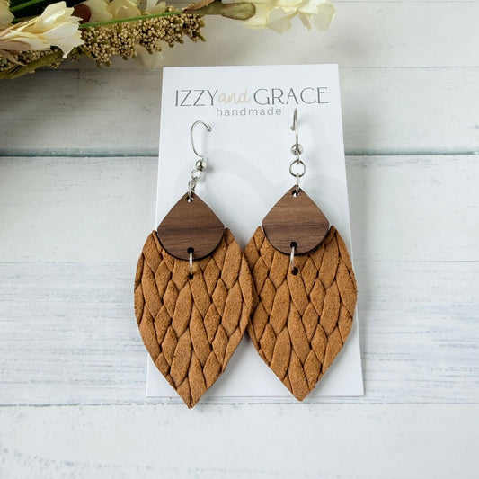 A pair of mustard woven leather dangle earrings with dark wood top caps and silver fishhook wires, displayed on a white card labeled 'IZZY and GRACE handmade' on a white wood background.